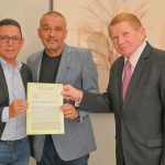 Três homens sorrindo segurando um documento oficial em uma sala com o documento sobre o novo Fórum de Silva