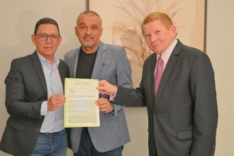 Três homens sorrindo segurando um documento oficial em uma sala com o documento sobre o novo Fórum de Silva