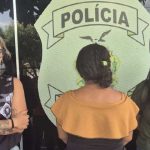 Três mulheres em frente a um emblema da polícia.