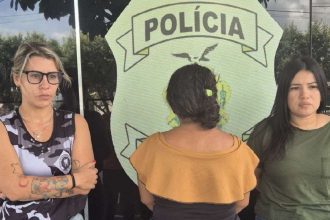 Três mulheres em frente a um emblema da polícia.
