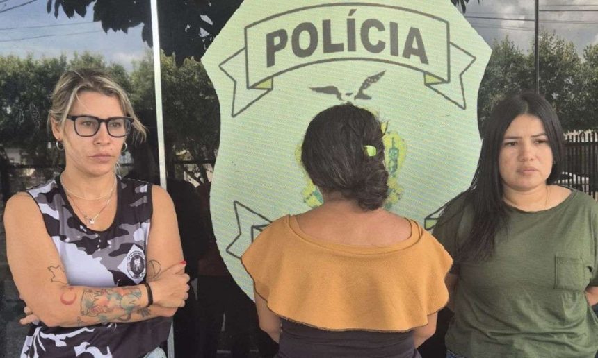 Três mulheres em frente a um emblema da polícia.