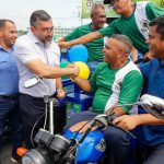 Wilson Lima entrega triciclos a produtores rurais, com balões e outros homens presentes.