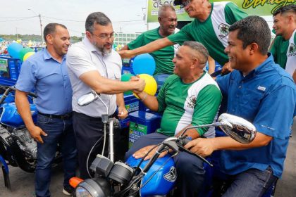 Wilson Lima entrega triciclos a produtores rurais, com balões e outros homens presentes.