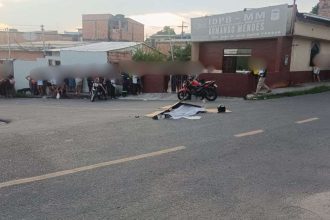 Acidente com vítima fatal envolvendo moto e ônibus. Cena no local com pessoas e veículos.