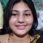 Adolescente sorrindo com cabelo escuro e colar.