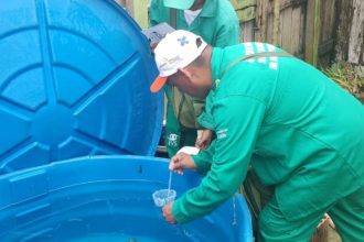 Agente da saúde coletando amostra de água em tanque azul, em meio a ações de combate à dengue no Amazonas.