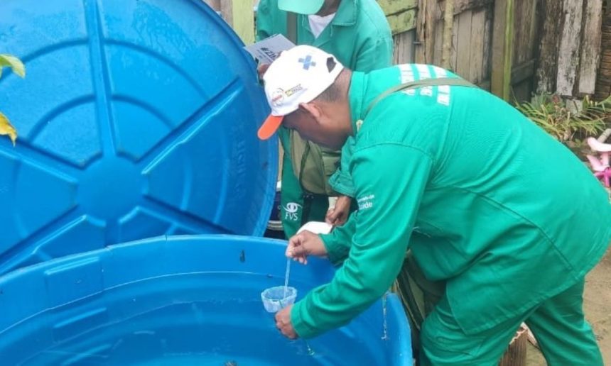 Agente da saúde coletando amostra de água em tanque azul, em meio a ações de combate à dengue no Amazonas.