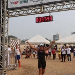 Atleta cruza a linha de chegada do Aquathlon Naval da Marinha do Brasil, com cronômetro marcando o tempo.