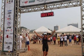 Atleta cruza a linha de chegada do Aquathlon Naval da Marinha do Brasil, com cronômetro marcando o tempo.