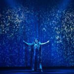 Atriz se apresenta em palco azul com efeitos, festival de teatro em Manaus.