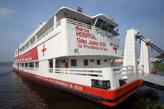 Barco hospital São João XXII, com a cruz vermelha, em um rio.