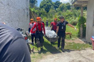 Bombeiros carregam corpo em maca em área de mata em comunidade.