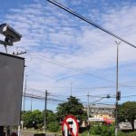 Câmeras de fiscalização eletrônica na Avenida do Turismo em Manaus, com céu azul e nuvens.