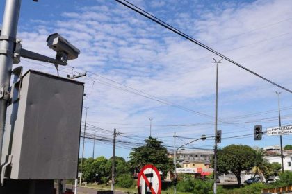 Câmeras de fiscalização eletrônica na Avenida do Turismo em Manaus, com céu azul e nuvens.
