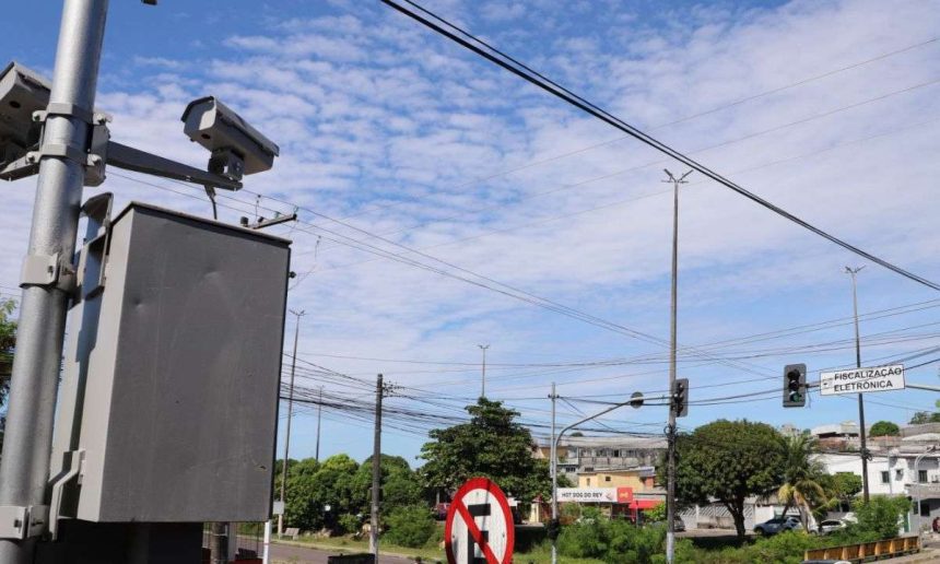 Câmeras de fiscalização eletrônica na Avenida do Turismo em Manaus, com céu azul e nuvens.