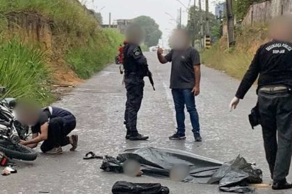 Cena de acidente com vítima fatal: homem coberto por lona ao lado de motocicleta e policiais.