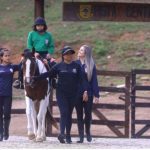 Criança com deficiência praticando equoterapia, com apoio de equipe