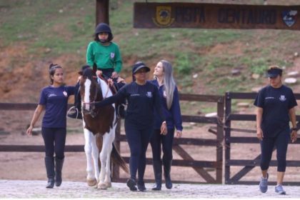 Criança com deficiência praticando equoterapia, com apoio de equipe