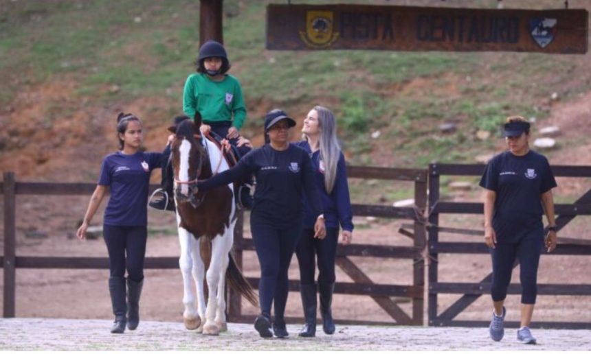 Criança com deficiência praticando equoterapia, com apoio de equipe