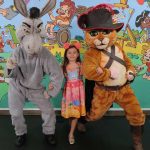 Criança com fantasias do Gato de Botas e Burro de Shrek em evento de doação de brinquedos em Manaus.