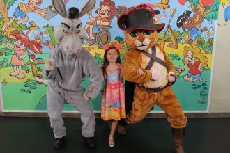 Criança com fantasias do Gato de Botas e Burro de Shrek em evento de doação de brinquedos em Manaus.
