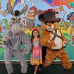 Criança posa com fantasias do Burro e Gato de Botas em evento.