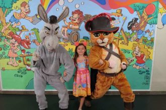 Criança posa com fantasias do Burro e Gato de Botas em evento.