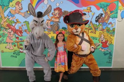 Criança posa com fantasias do Burro e Gato de Botas em evento.