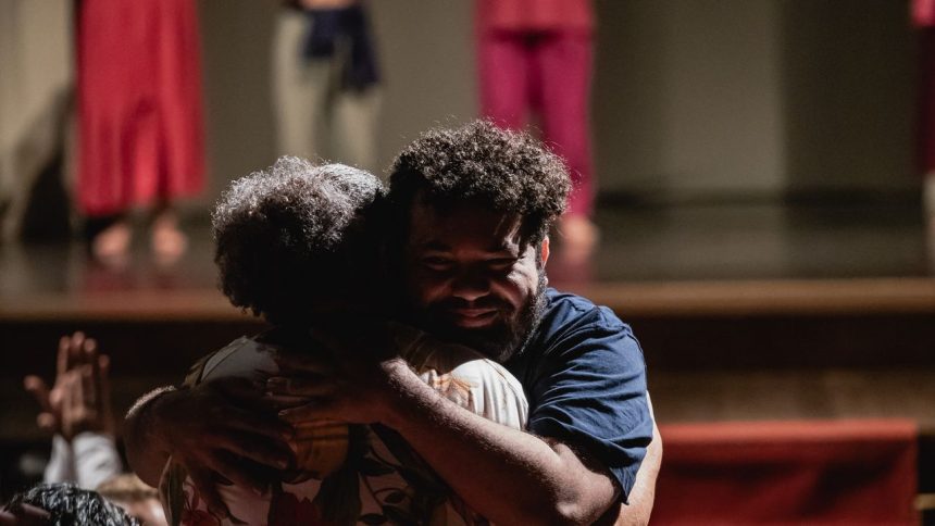 Dois homens se abraçam no palco, com outros atores ao fundo, em evento do Ateliê 23.