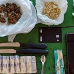 Drogas, facas, cartão de crédito, comprimidos e celular sobre mesa.