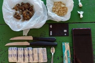 Drogas, facas, cartão de crédito, comprimidos e celular sobre mesa.