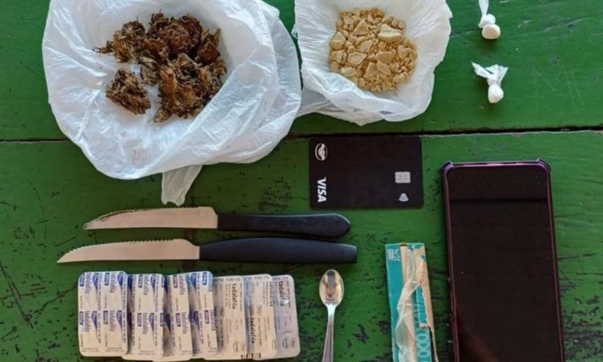 Drogas, facas, cartão de crédito, comprimidos e celular sobre mesa.