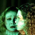 Duas mulheres com maquiagem teatral em tons de verde, em um palco