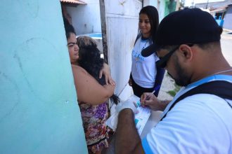 Equipe de vacinação animal em Manaus, com uma pessoa segurando um cachorro e outra preenchendo formulário.