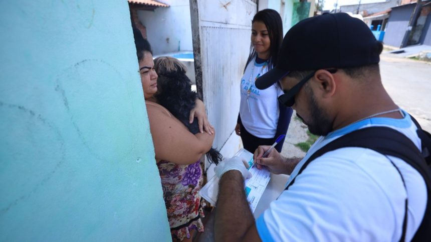Equipe de vacinação animal em Manaus, com uma pessoa segurando um cachorro e outra preenchendo formulário.
