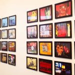 Exposição de arte com várias molduras pretas penduradas em uma parede branca, com obras de arte variadas.