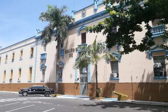 Fachada do Colégio Militar de Manaus em dia ensolarado, com carro e palmeiras.