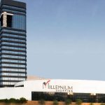 Fachada do Millennium Shopping, com edifícios modernos e céu azul ao fundo.