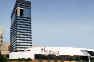 Fachada do Millennium Shopping, com edifícios modernos e céu azul ao fundo.