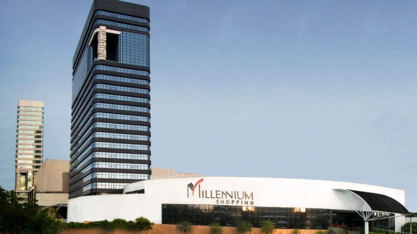 Fachada do Millennium Shopping, com edifícios modernos e céu azul ao fundo.