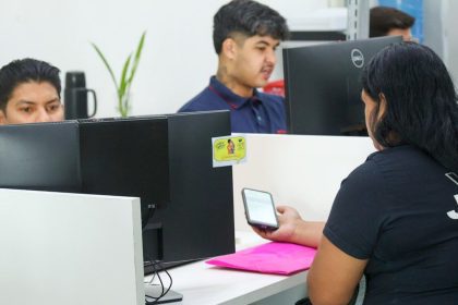 Funcionários em escritório, trabalhando em computadores e verificando um smartphone. Cena de escritório.