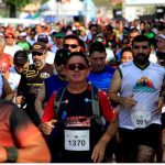 Grande número de pessoas correndo em uma maratona, com destaque para atletas com números de identificação.
