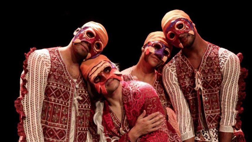 Grupo de dançarinos com máscaras coloridas e roupas tradicionais se apresenta no palco.