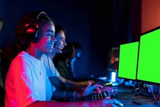 Grupo de jovens gamers com fones de ouvido, jogando em computadores com telas verdes.