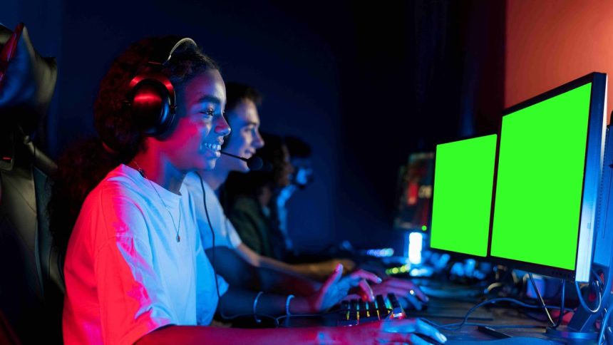 Grupo de jovens gamers com fones de ouvido, jogando em computadores com telas verdes.