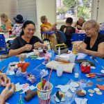 Grupo de mulheres em curso de artesanato, focadas em costura criativa, com materiais e projetos sobre a mesa.