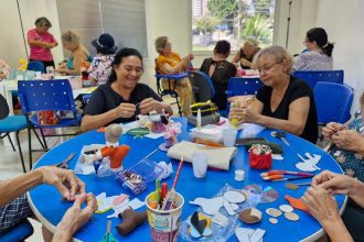 Grupo de mulheres em curso de artesanato, focadas em costura criativa, com materiais e projetos sobre a mesa.