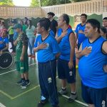 Grupo de pessoas, algumas em cadeiras de rodas, com a mão no peito, em um evento da APAE Manaus.