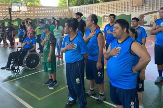 Grupo de pessoas, algumas em cadeiras de rodas, com a mão no peito, em um evento da APAE Manaus.