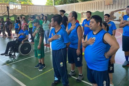 Grupo de pessoas, algumas em cadeiras de rodas, com a mão no peito, em um evento da APAE Manaus.